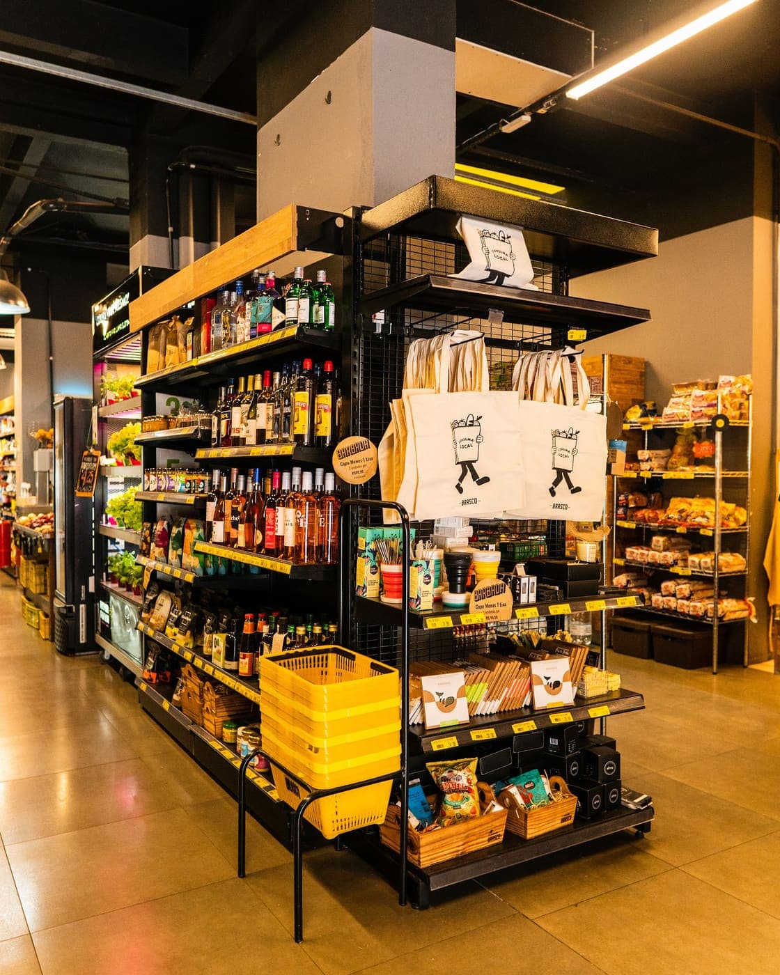 Corredor da mercearia do Brasco Florêncio, com vinhos, ecobags e cestinhas amarelas.
