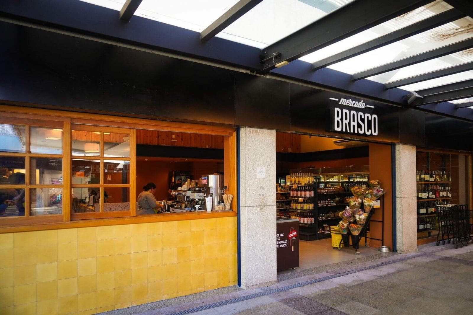 Fachada do Brasco no Viva Open Mall: balcão de café com azulejos amarelos, letreiro Mercado Brasco e a mercearia ao fundo.